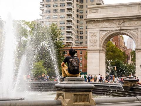 Student sitting near fountain in front of Washington Square Arch