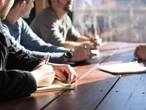 People sitting on chair in front of table while holding pens during daytime