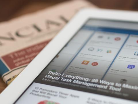 A newspaper and computer tablet laying on a table