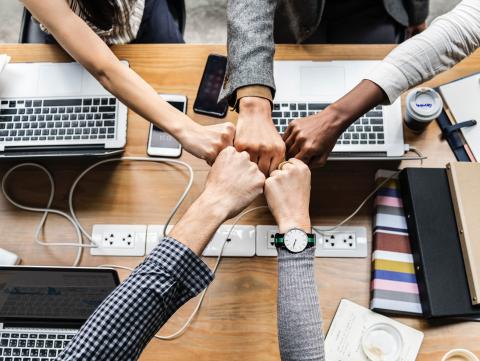 Five people doing fistbumps over a table with laptops