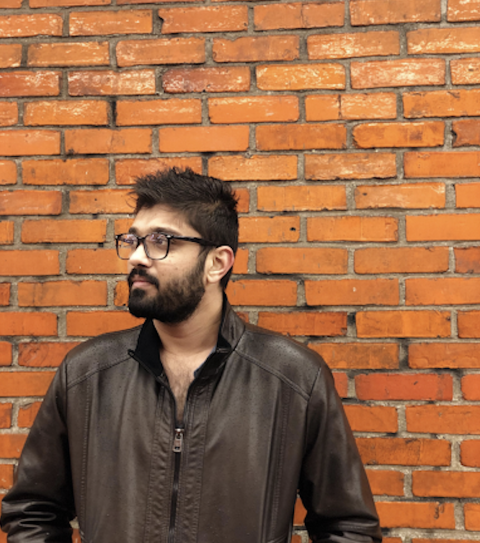 Devarshi standing in front of a red brick wall