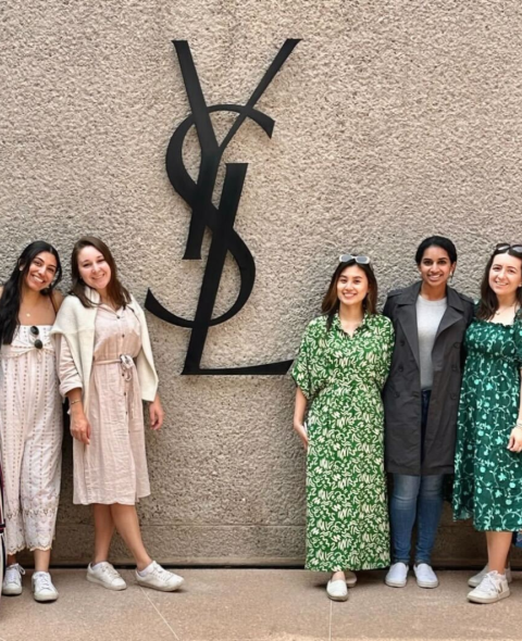 7 students stand outside the YSL office - a concrete building with a large YSL logo