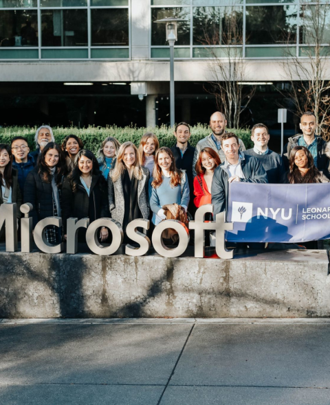 The Tech MBA cohort stands around the Microsoft sign in San Francisco while holding an NYU Stern MBA flag.