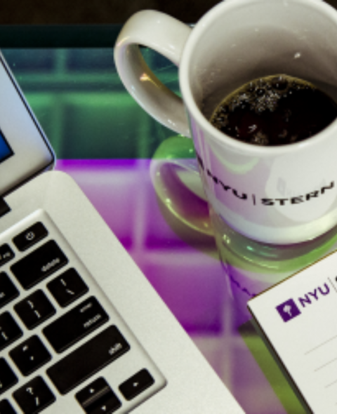 A photo of a laptop, notepad, and mug. The NYU Stern logo is on the notepad and mug.