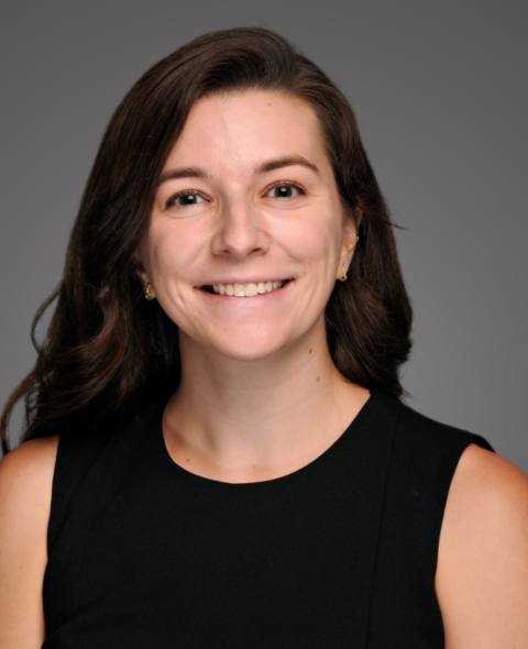 Kaitlyn smiles at the camera with a black shirt and brown hair against a gray background.