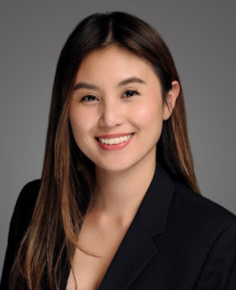 Katelyn has long brown hair and wears a black blazer against a gray background. She smiles at the camera.