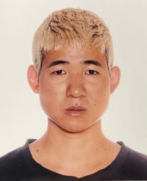 Timothy has bleached hair and stares directly at the camera. He wears a black shirt against a white background.