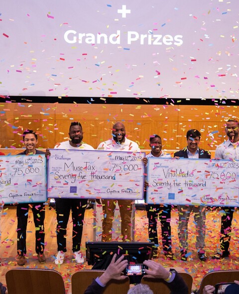 Winners stand on stage with their prize checks as confetti falls