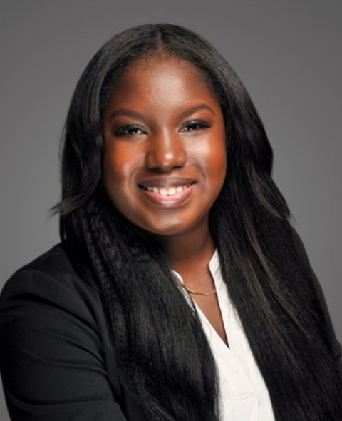 A portrait of Fatim Lelenta - A black woman in a suit smiling at the camera