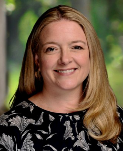 A portrait of Genevieve Kenny Boron - A white woman smiling a the camera in a flower shirt