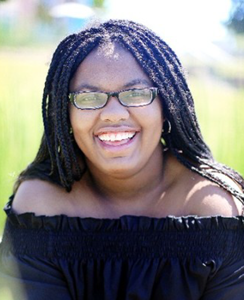 A portrait of Nik Wesson - A black woman in a black shirt smiling at the camera