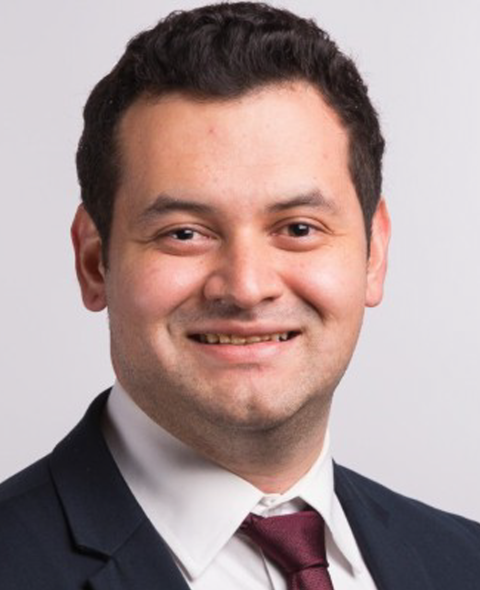 A portrait of Yaniv Kleinman - A dark haired latine man in a suit smiling at the camera