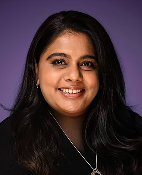 Nourine is an Indian American woman with dark black hair, dark shirt, and silver necklace. She is on a purple background.
