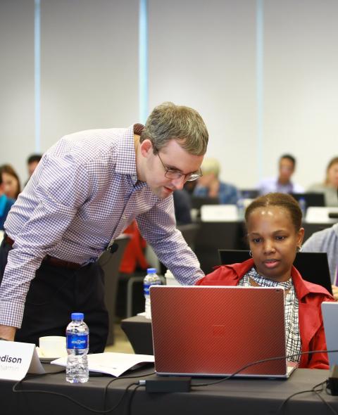 Professor looks at laptop with two students in a class setting
