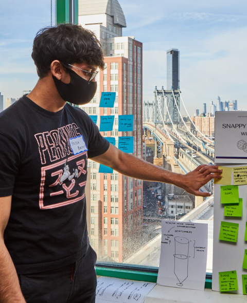 Student with team poster in front of window overlooking DUMBO