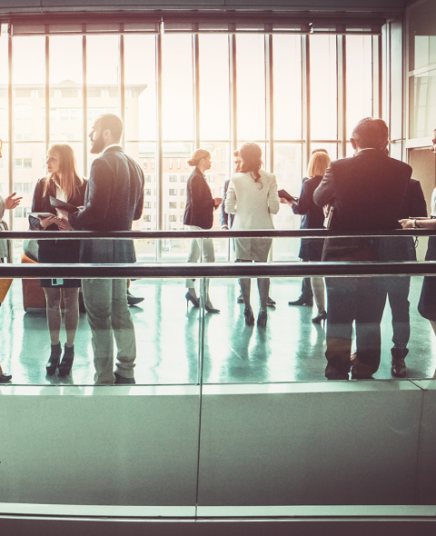 groups of businesspeople chatting in a large room with floor to ceiling windows