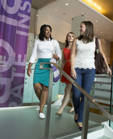 three women in business casual attire looking at each other as they descend a staircase