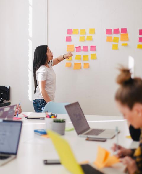 Person gestures to sticky notes on a wall during a meeting