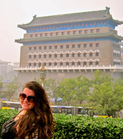student with long brown hair posing in front of a large building in china