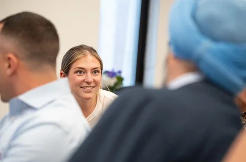 A feminine-presenting person with light skin and hair smiles intently at a partner whose back is to the camera.