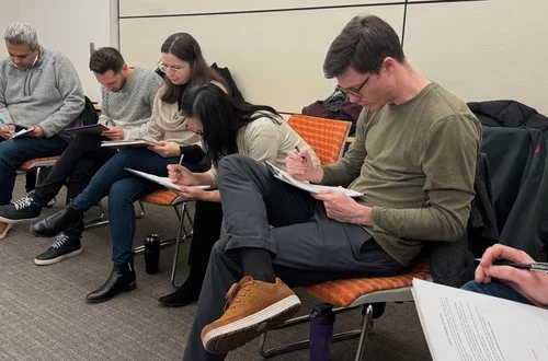 Five students sit in a row writing out responses on pieces of paper that sit on their laps.