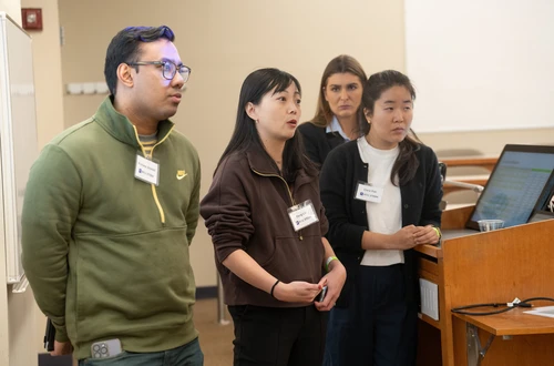 A group of four students stand at the front of the classroom expectantly. 