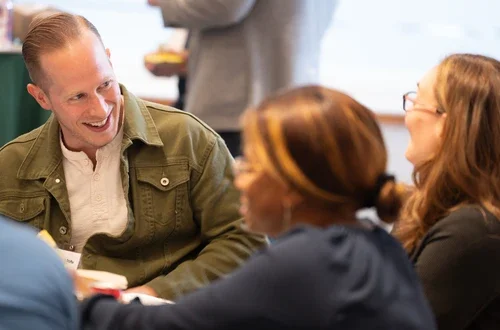 A group of students sit around a table, laughing.