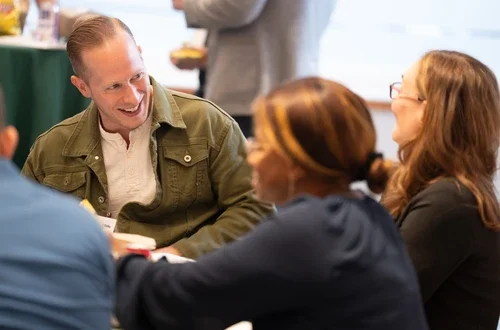 A group of students sit around a table, laughing.