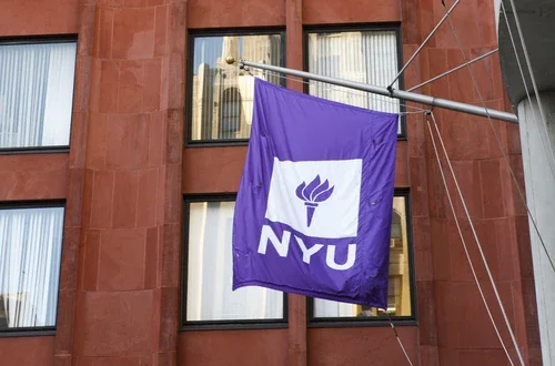 Two NYU Flags flying in front of Stern buildings
