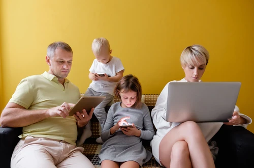 A family sitting together on a couch. Each person is looking at a smartphone, computer or electronic notebook