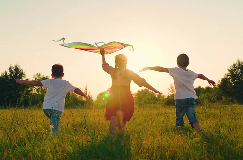 Three children running through a field with a kite