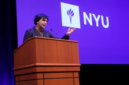 Filmmaker M. Night Shyamalan speaking at a podium in front of NYU logo background