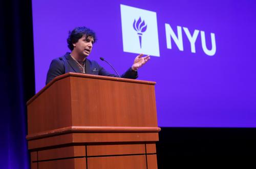 Filmmaker M. Night Shyamalan speaking at a podium in front of NYU logo background