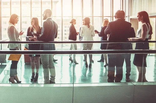 groups of businesspeople chatting in a large room with floor to ceiling windows