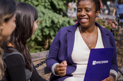 woman holding an nyu stern-labeled folder speaking to other women on a park bench