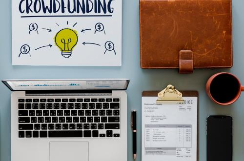 MacBook Pro near neatly organized click pen, clipboard, coffee, phone, file holder, and doodle with the word "crowdfunding" 