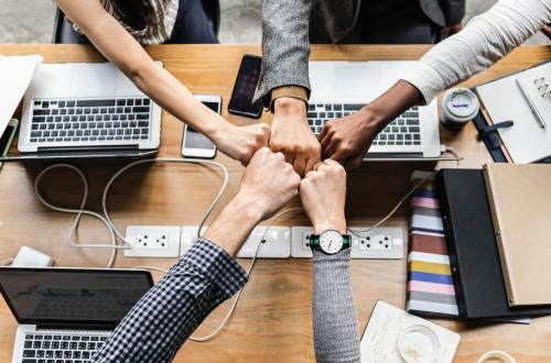 Five people doing fistbumps over a table with laptops