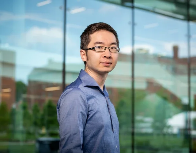 Photo of Professor Qiaochu Wang in front of a glass building