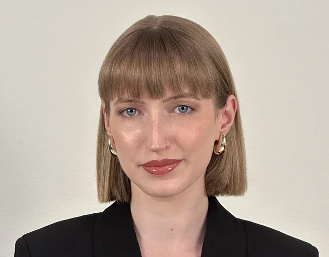A feminine-presenting person with light skin and hair smiles softly into the camera. She's wearing an oversized blazer, and her hair is in a bob.