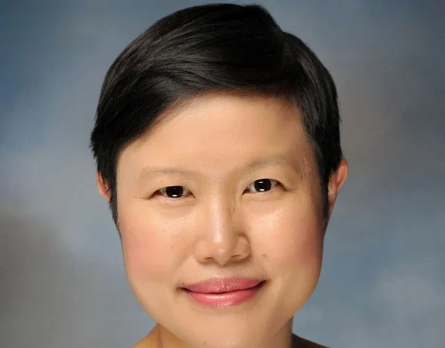 A feminine-presenting person with glasses, short black hair, and medium skin smiles into the camera.