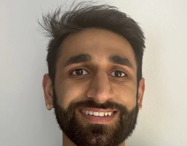 A person with caramel skin and a short black goatee smiles directly into the camera. His name is Sid.