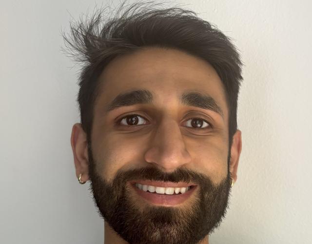 A person with caramel skin and a short black goatee smiles directly into the camera. His name is Sid.