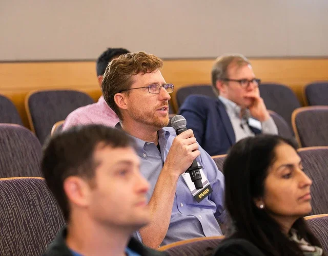 Robert Seamans sitting among the crowd in a lecture hall holding a microphone.