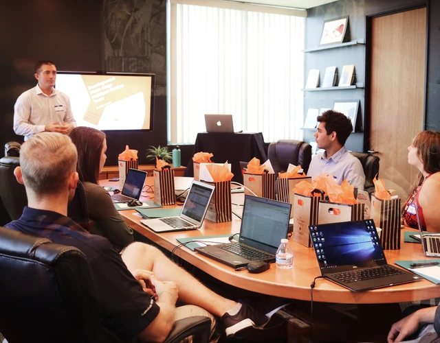 A group of people sitting around a conference table listening to a man presenting at the head of the table
