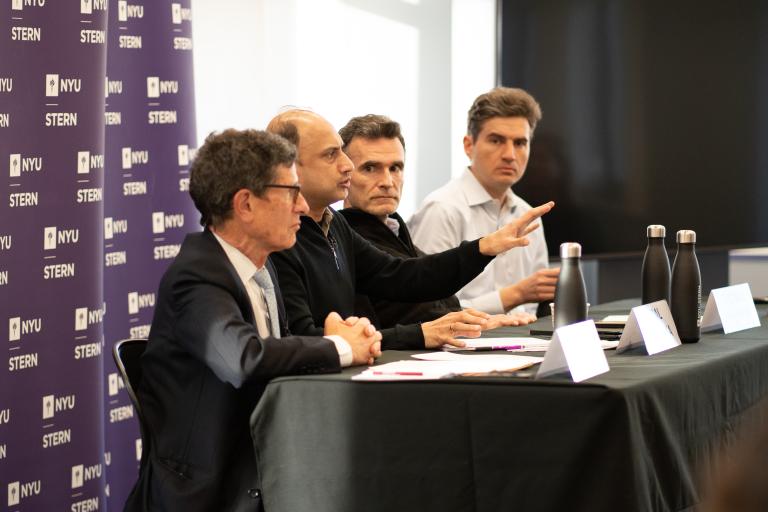 professors richard berner, viral acharya, thomas philippon, and alexi savov sitting at a table while viral acharya speaks to a crowd