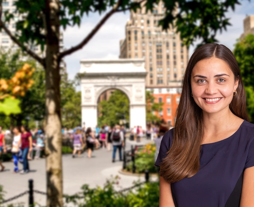 Female student with brown hair and blue dress in front of a blurred background of Washington Square Park