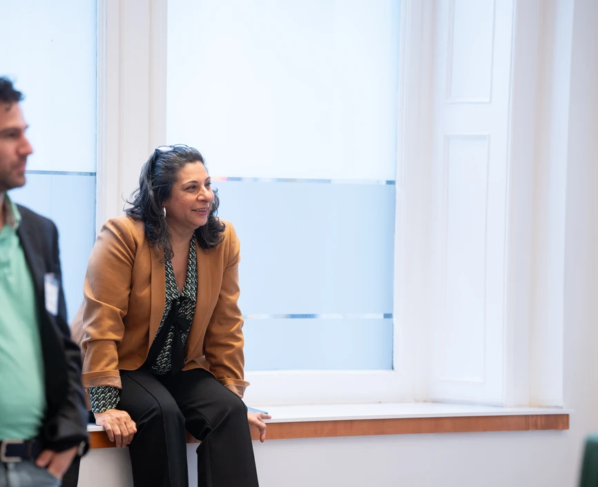 Professor Dolly Chugh sits on a windowsill and, with a smile on her face, attentively listens to a student, who is out of frame.