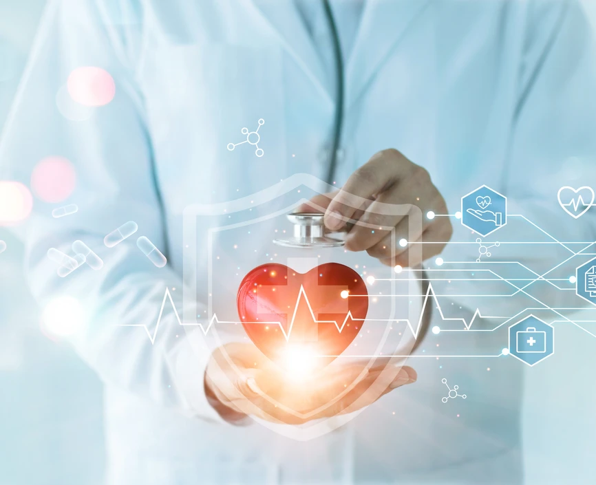 Person in white medical coat holds illuminated image of a heart in his palm. Blurred medical floor with people in the background. 