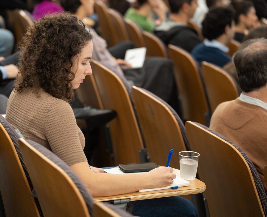 A woman writes in her notebook in a lecture hall
