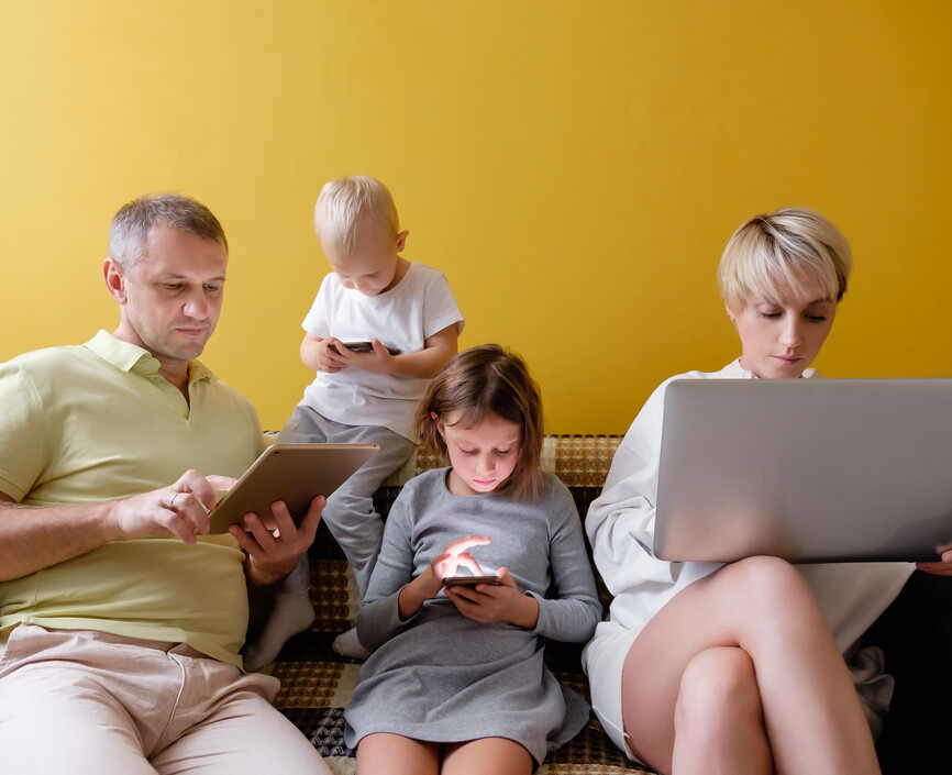 A family sitting together on a couch. Each person is looking at a smartphone, computer or electronic notebook